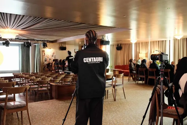 A Centauri crew member filming a room of guests from behind a tripod.