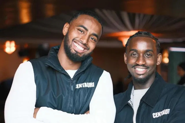Two of the crew in branded jackets at a client event, laughing.