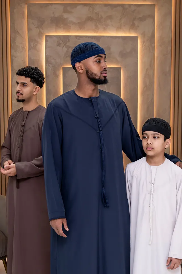 Three generations in navy, brown and white thobes in a warmly lit room.