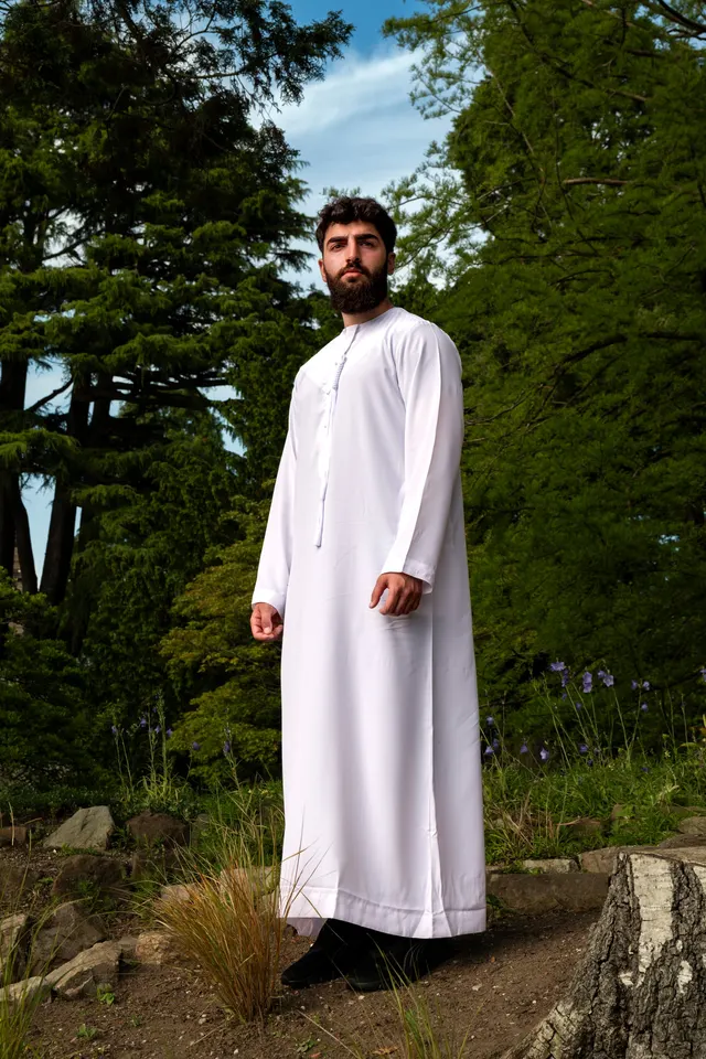 A man in a white thobe standing among trees in a park.
