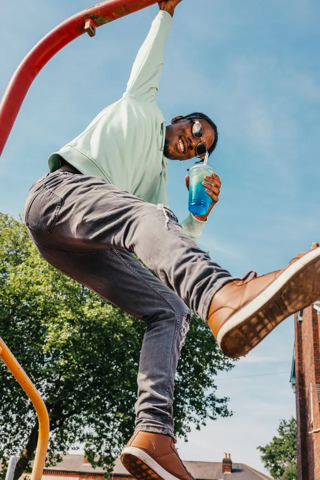A man hanging off a playground frame with a blue slush drink.